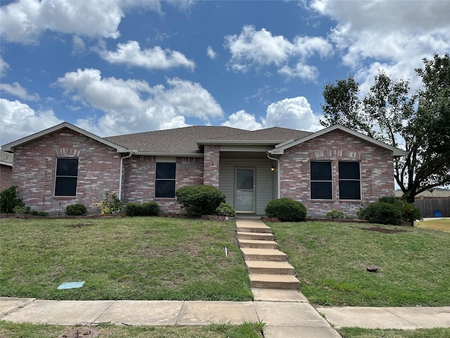 ranch-style home with roof with shingles, a front yard, and brick siding