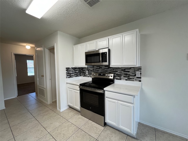 kitchen with appliances with stainless steel finishes, tasteful backsplash, white cabinetry, and light tile patterned flooring