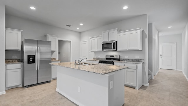 kitchen featuring light stone countertops, stainless steel appliances, a center island with sink, and white cabinetry