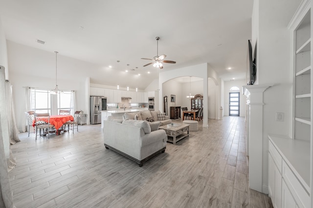 living room featuring lofted ceiling, ceiling fan with notable chandelier, and light hardwood / wood-style floors