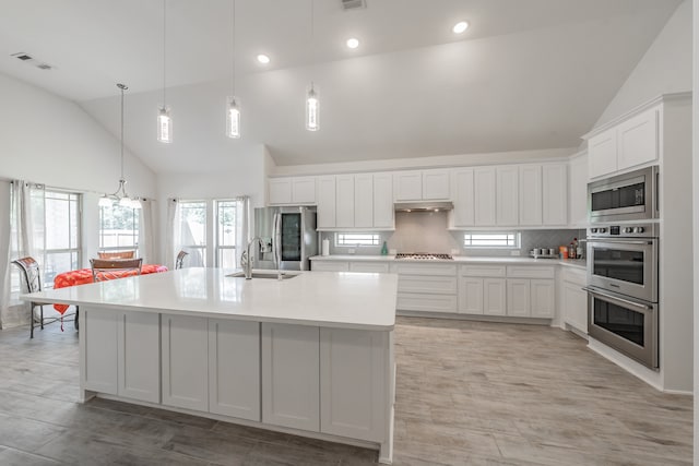 kitchen featuring an island with sink, pendant lighting, stainless steel appliances, and high vaulted ceiling