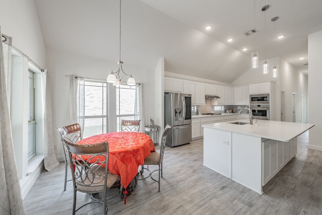 kitchen with high vaulted ceiling, sink, appliances with stainless steel finishes, a center island with sink, and white cabinets