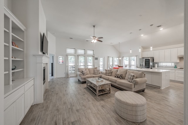 living room with high vaulted ceiling, ceiling fan, and light hardwood / wood-style flooring