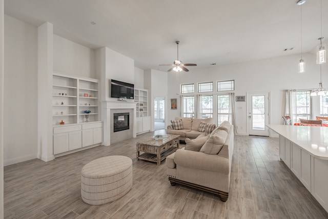 living room with a high ceiling, ceiling fan with notable chandelier, and light wood-type flooring