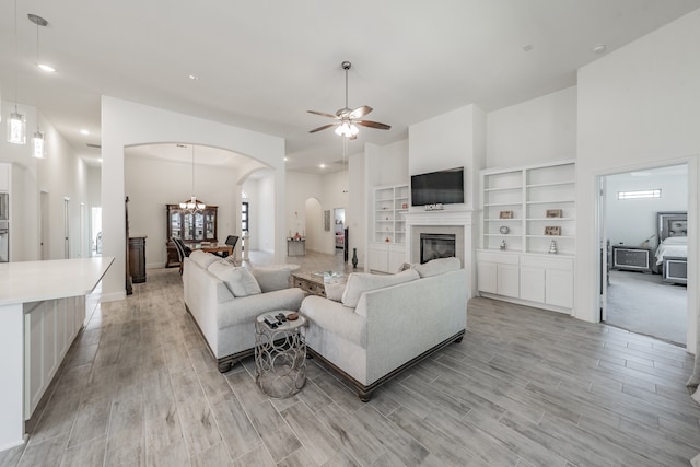 living room featuring ceiling fan with notable chandelier, light wood-type flooring, and a towering ceiling