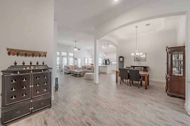 interior space featuring ceiling fan with notable chandelier, a tray ceiling, and light hardwood / wood-style floors