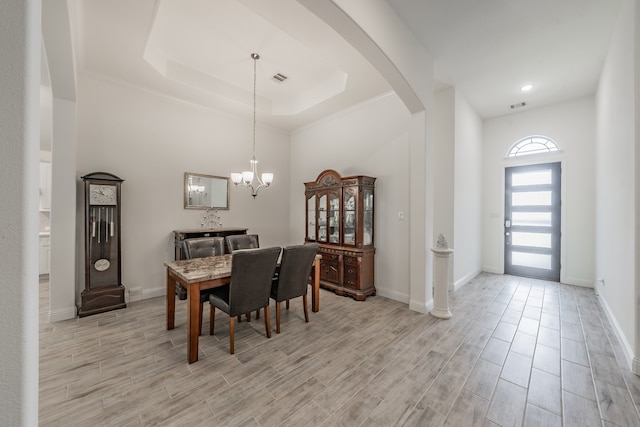 dining area with a tray ceiling, light hardwood / wood-style floors, and a chandelier