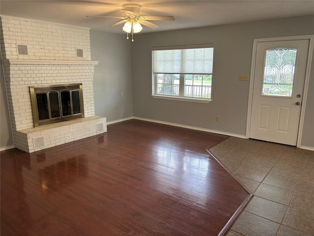 unfurnished living room with a brick fireplace, plenty of natural light, ceiling fan, and dark tile patterned flooring