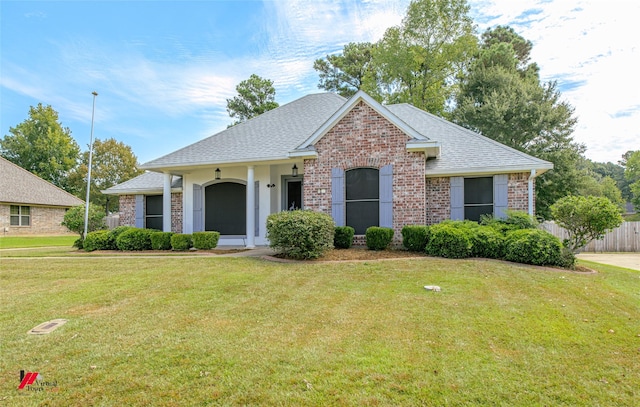 ranch-style house with brick siding, a front lawn, a shingled roof, and fence