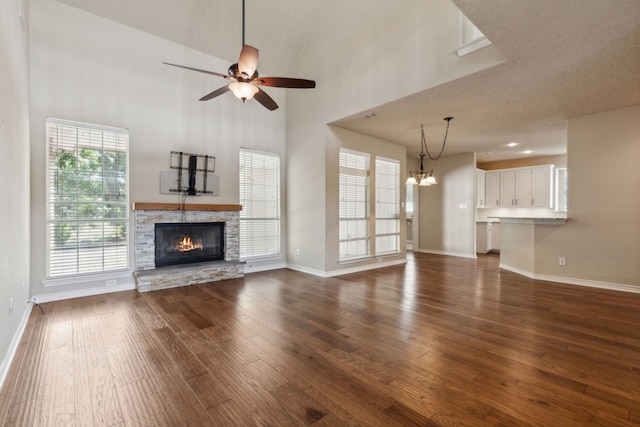 unfurnished living room with a fireplace, ceiling fan with notable chandelier, wood-type flooring, high vaulted ceiling, and a textured ceiling