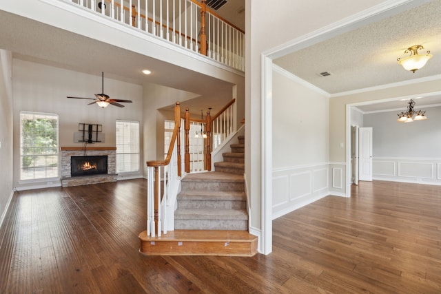 staircase featuring a fireplace, a high ceiling, ceiling fan with notable chandelier, a textured ceiling, and hardwood / wood-style flooring