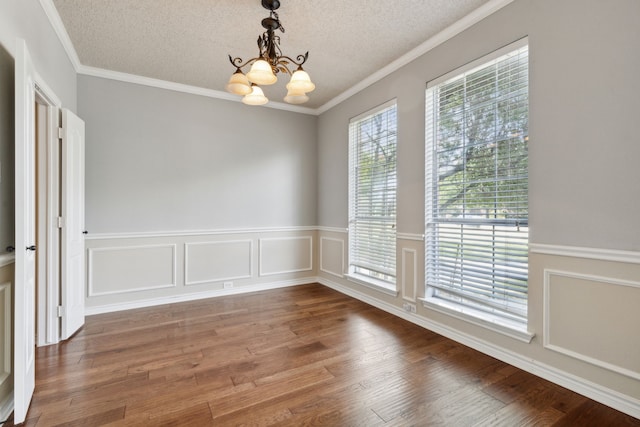 unfurnished dining area featuring a textured ceiling, ornamental molding, a notable chandelier, and wood-type flooring