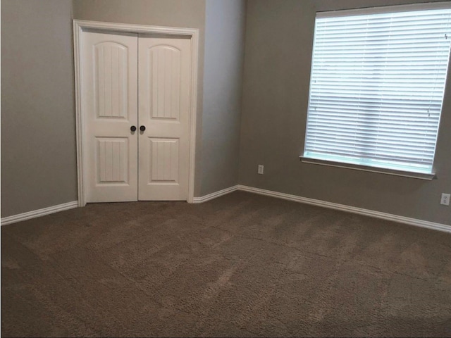 unfurnished bedroom featuring dark carpet and multiple windows