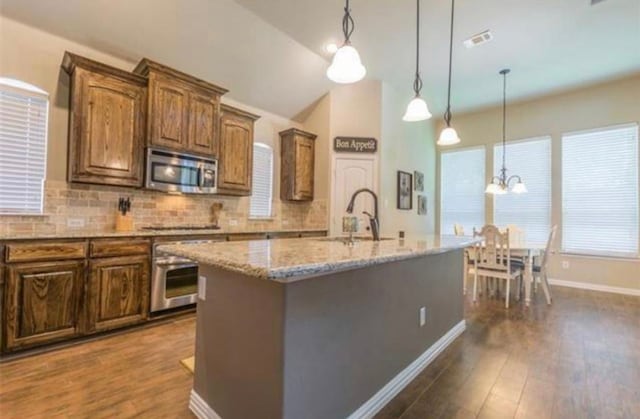 kitchen featuring light stone countertops, stainless steel appliances, a notable chandelier, sink, and an island with sink