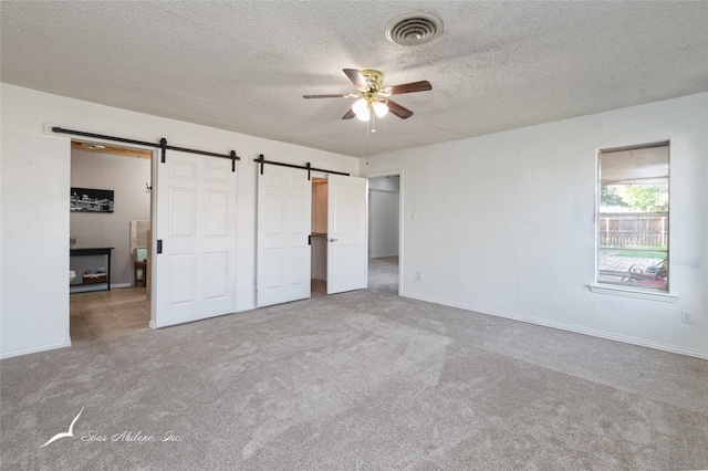 unfurnished bedroom featuring a barn door, carpet floors, and ceiling fan