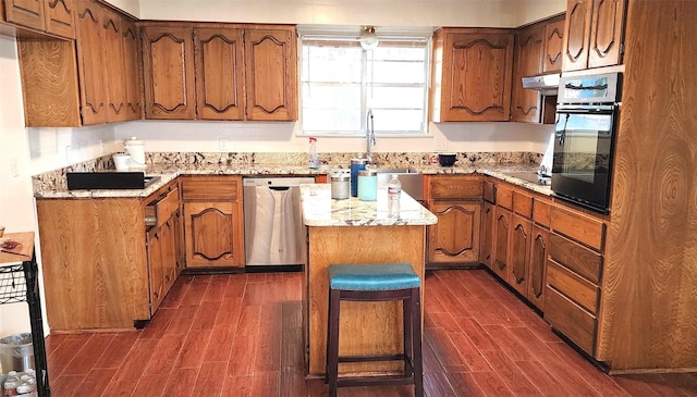 kitchen featuring a breakfast bar, sink, a center island, light stone countertops, and black appliances