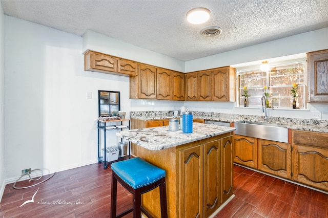 kitchen with a textured ceiling, sink, dark wood-type flooring, and a kitchen island