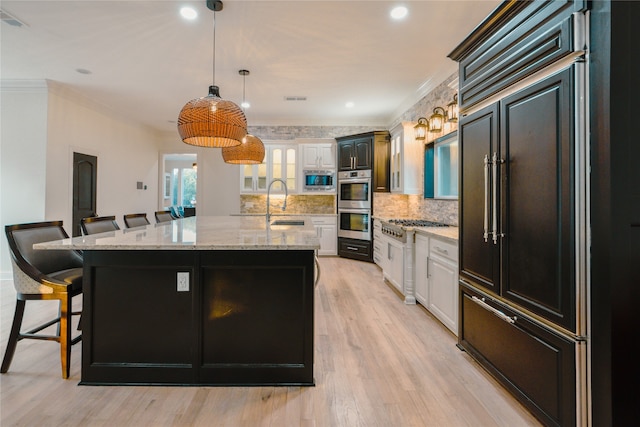 kitchen featuring a kitchen bar, ornamental molding, a kitchen island with sink, and light hardwood / wood-style flooring