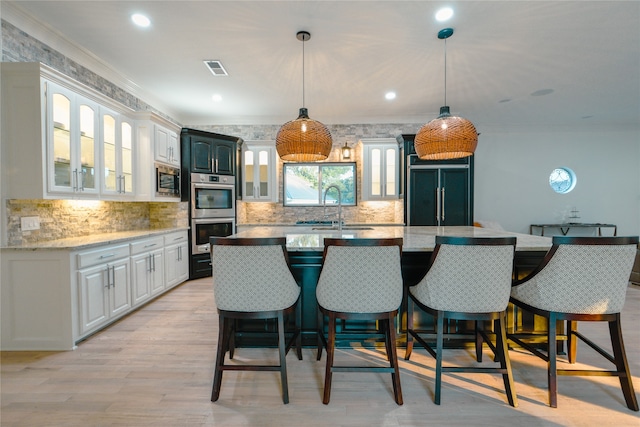 kitchen with appliances with stainless steel finishes, an island with sink, sink, light wood-type flooring, and white cabinets