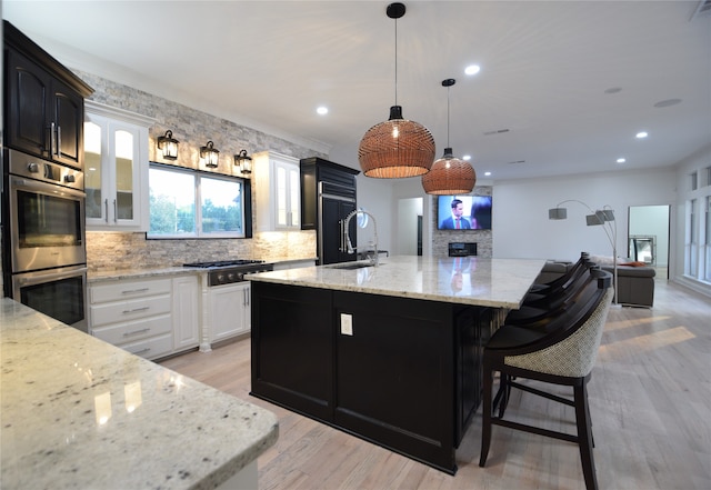 kitchen with a spacious island, appliances with stainless steel finishes, sink, light stone counters, and light wood-type flooring