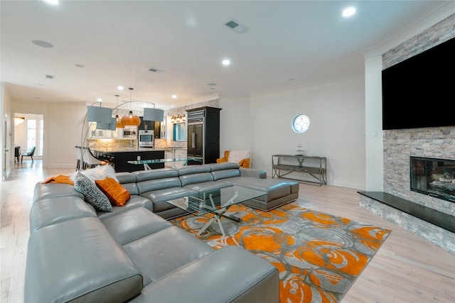 living room with crown molding, a stone fireplace, and light wood-type flooring