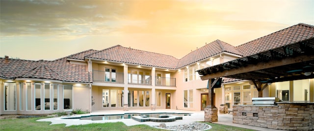 back house at dusk with area for grilling, a patio area, a balcony, and a pool with hot tub