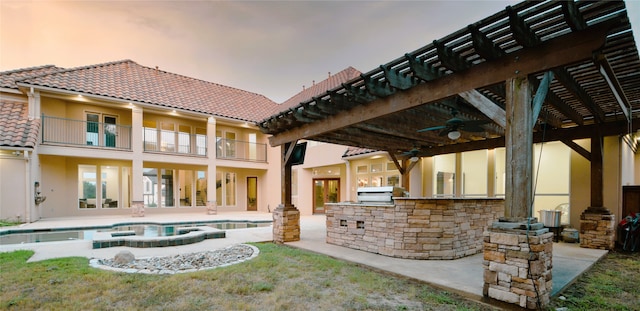 back of house featuring a balcony, a patio area, an outdoor kitchen, a yard, and ceiling fan