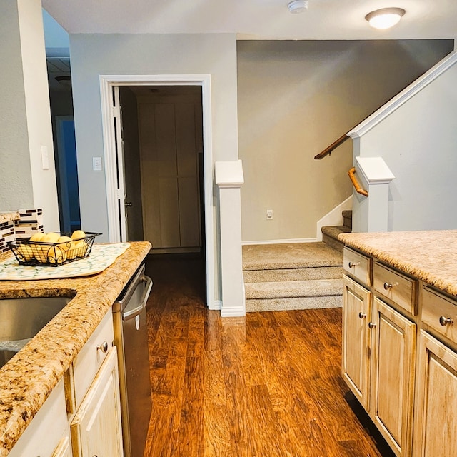 kitchen with light stone countertops, dark wood-type flooring, stainless steel dishwasher, and light brown cabinets