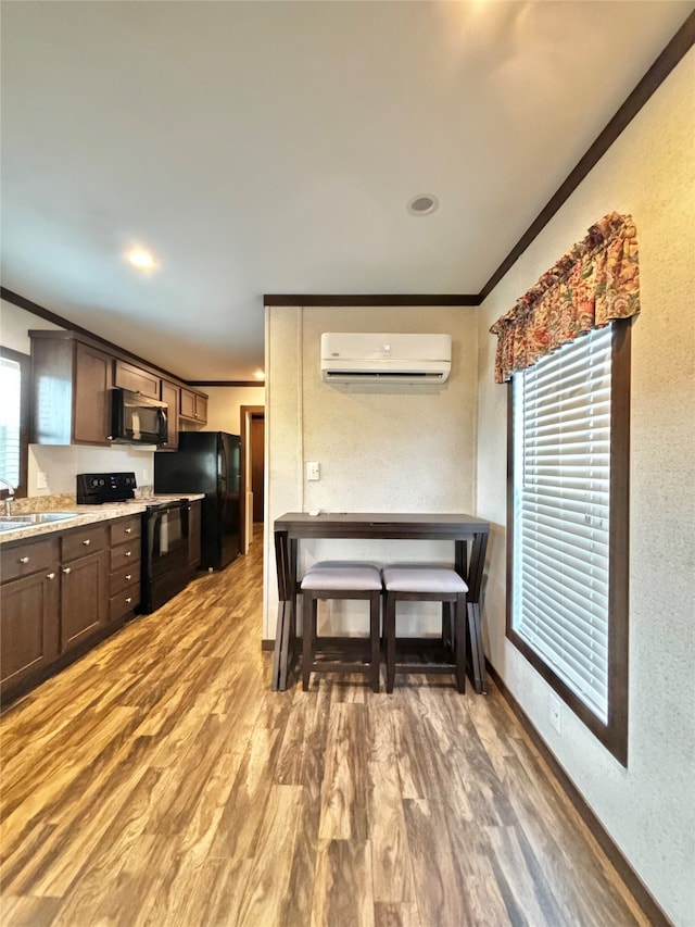 kitchen featuring crown molding, black appliances, an AC wall unit, and hardwood / wood-style flooring