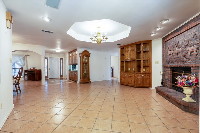 tiled living room with a tray ceiling, an inviting chandelier, and a brick fireplace