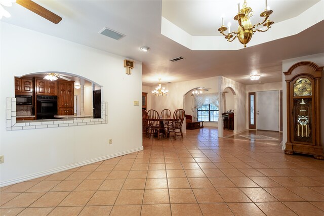 tiled foyer entrance featuring ceiling fan with notable chandelier and a tray ceiling