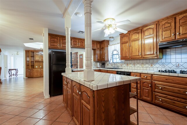 kitchen with light tile patterned floors, a kitchen island, ceiling fan, tile counters, and decorative backsplash