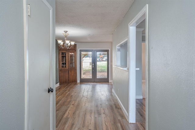 hall with a textured ceiling, hardwood / wood-style floors, a chandelier, and french doors