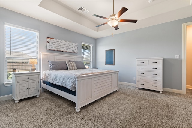 bedroom featuring light carpet, multiple windows, a tray ceiling, and ceiling fan