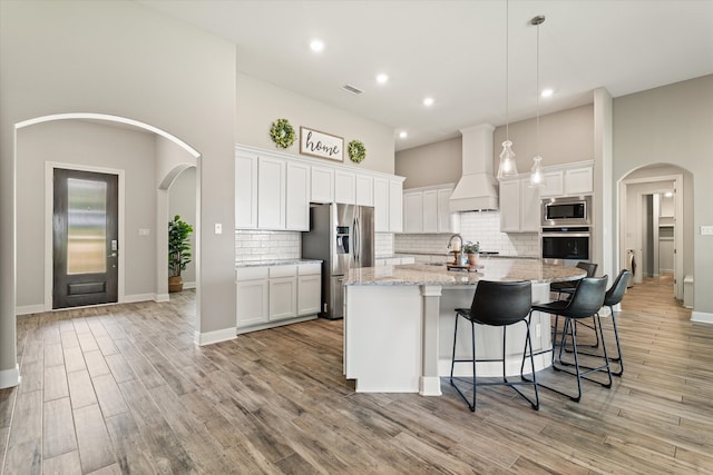 kitchen with a center island with sink, premium range hood, stainless steel appliances, and white cabinets