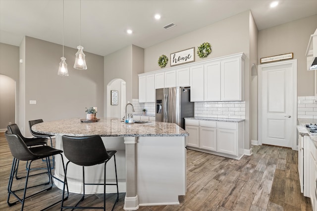 kitchen with a kitchen island with sink, stainless steel refrigerator with ice dispenser, white cabinetry, light hardwood / wood-style floors, and tasteful backsplash