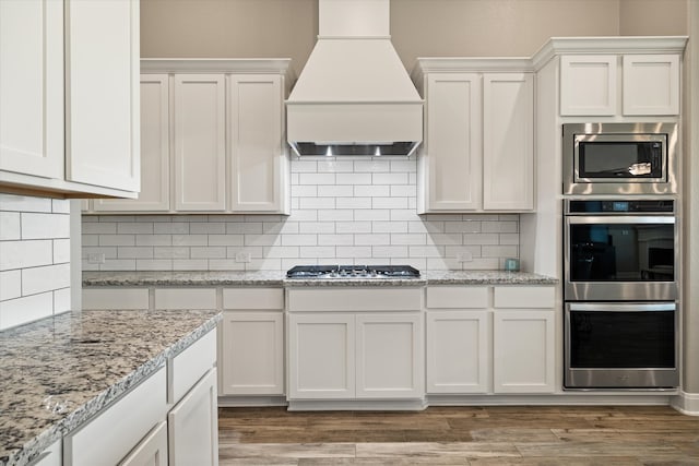 kitchen with light wood-type flooring, tasteful backsplash, custom exhaust hood, and white cabinets