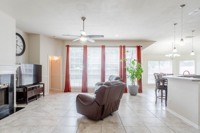 living room with ceiling fan with notable chandelier, light tile patterned floors, a tiled fireplace, and sink