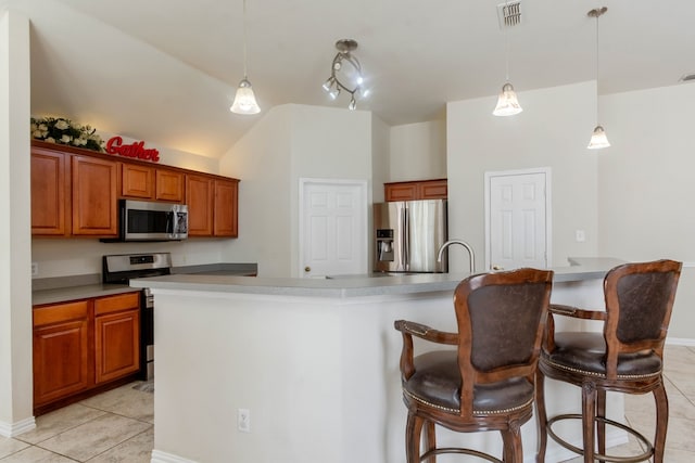 kitchen with light tile patterned floors, appliances with stainless steel finishes, pendant lighting, a kitchen island with sink, and a breakfast bar