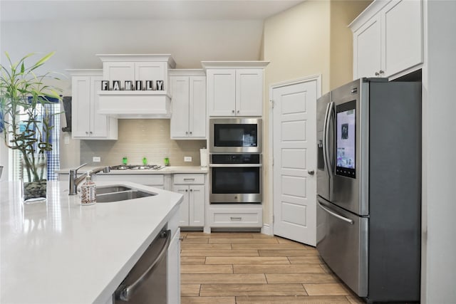 kitchen with light wood-type flooring, tasteful backsplash, sink, appliances with stainless steel finishes, and white cabinets