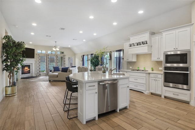 kitchen with a kitchen island with sink, white cabinetry, light hardwood / wood-style flooring, appliances with stainless steel finishes, and lofted ceiling