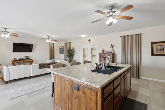 kitchen featuring french doors, light stone countertops, sink, ceiling fan, and a kitchen island with sink