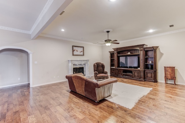 living room with ornamental molding, light wood-type flooring, ceiling fan, and a fireplace