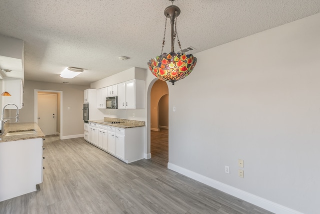 kitchen with light wood-type flooring, a textured ceiling, sink, hanging light fixtures, and white cabinets