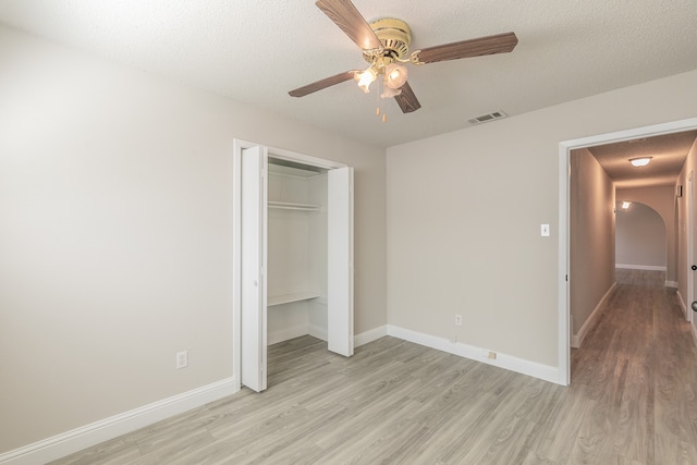 unfurnished bedroom with light wood-type flooring, a textured ceiling, ceiling fan, and a closet