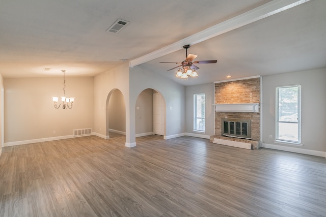 unfurnished living room with ceiling fan with notable chandelier, a fireplace, wood-type flooring, and a healthy amount of sunlight