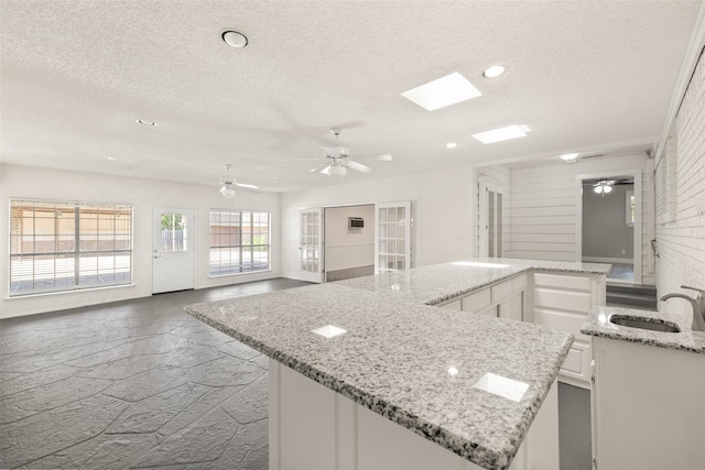 kitchen with a textured ceiling, ceiling fan, sink, and white cabinets