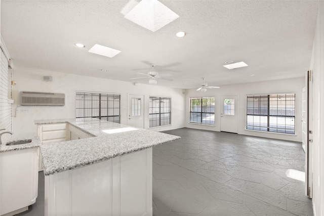 kitchen featuring a wall mounted AC, a textured ceiling, a skylight, light stone counters, and ceiling fan