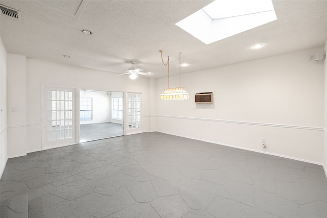 empty room featuring a skylight, ceiling fan, a wall mounted air conditioner, and a textured ceiling