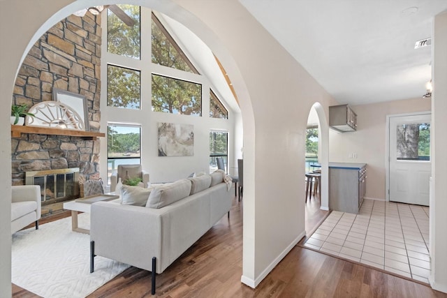 living room with hardwood / wood-style flooring, a stone fireplace, a wealth of natural light, and high vaulted ceiling